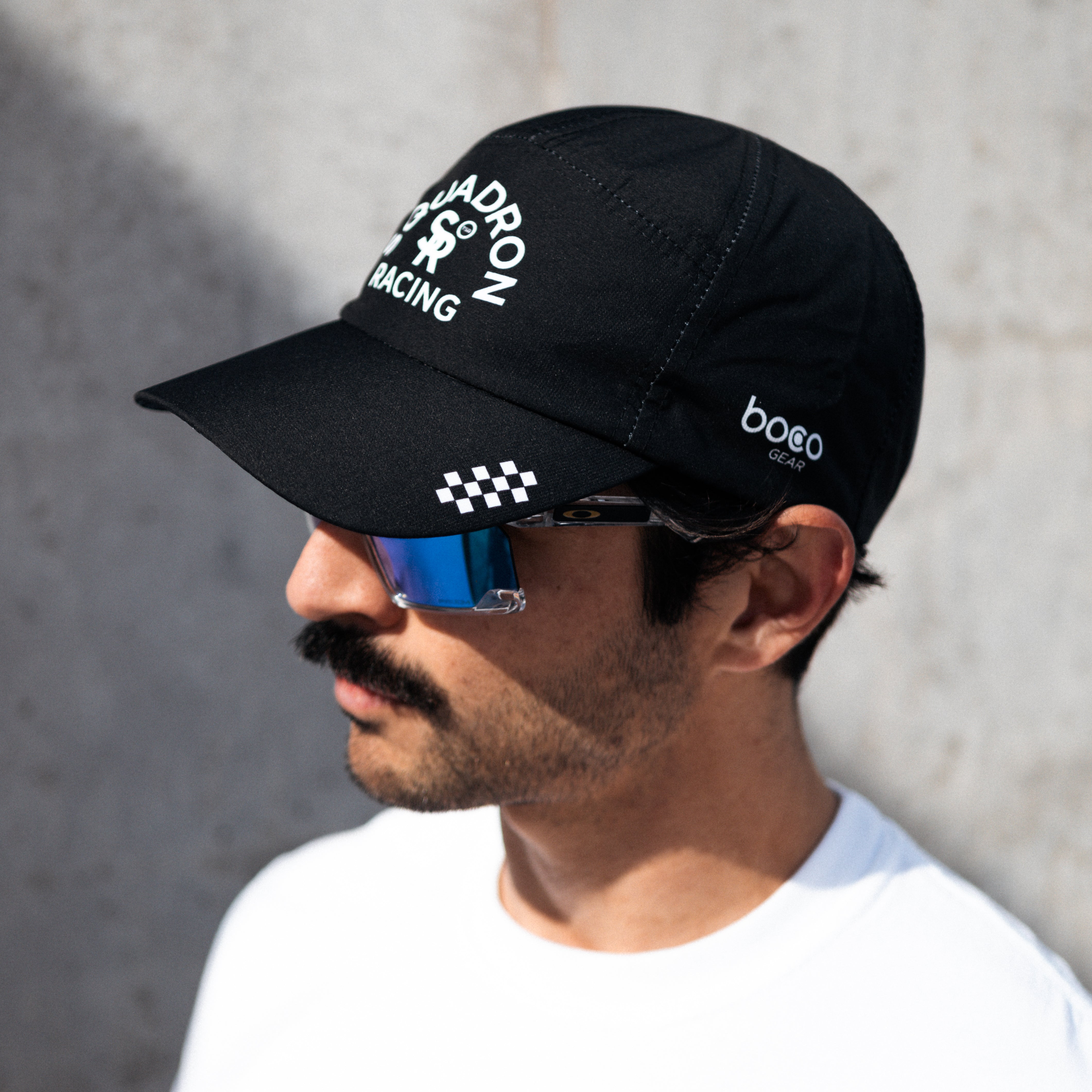 Athlete wearing a black squadron racing hat, looking away against a gray background. 